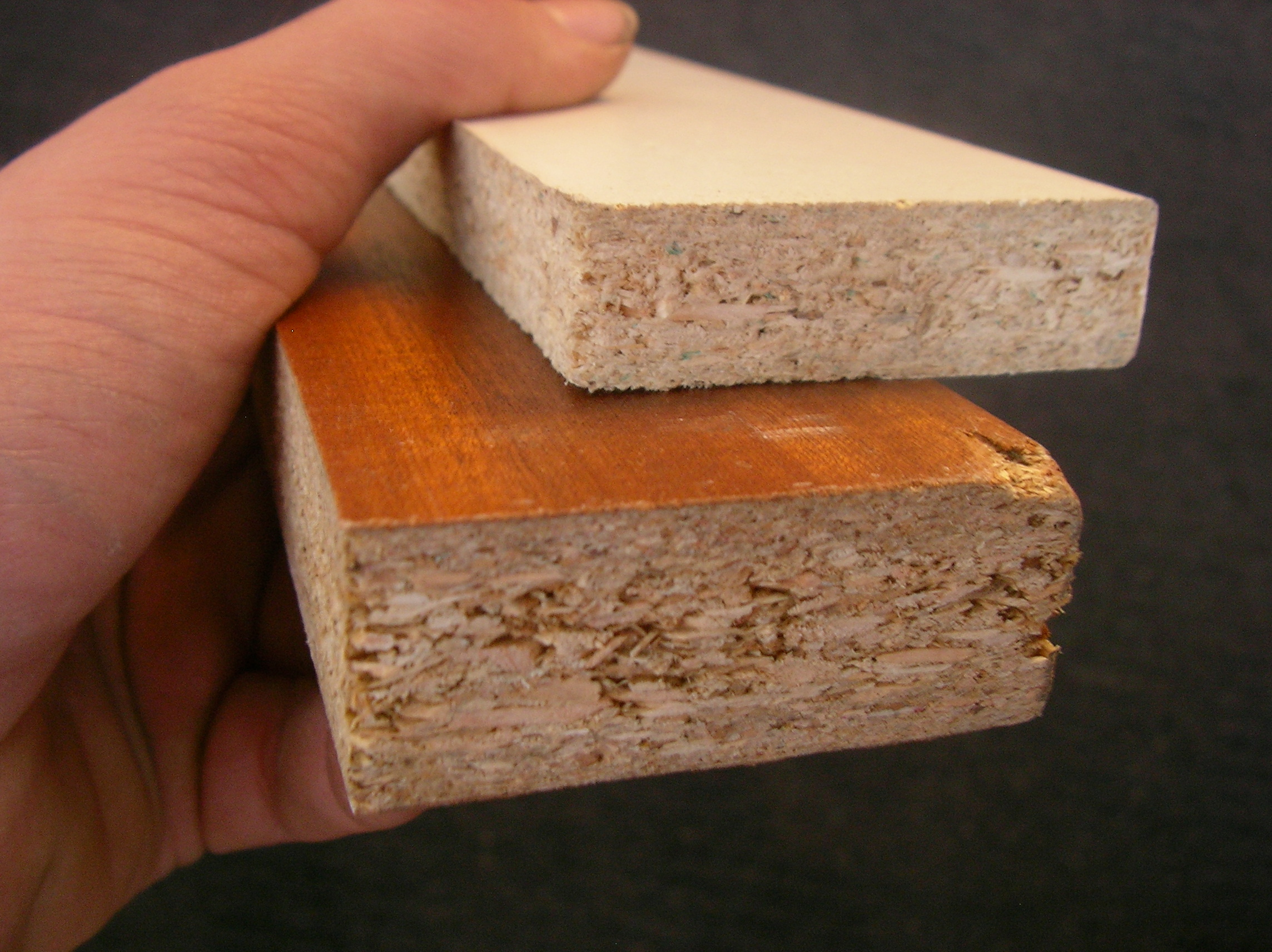 Hand holds two pieces on particle board; closeup of edge - photo