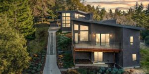 exterior view of modern home on wooded hillside; accessory dwelling unit in the rear; light glow from within – photo