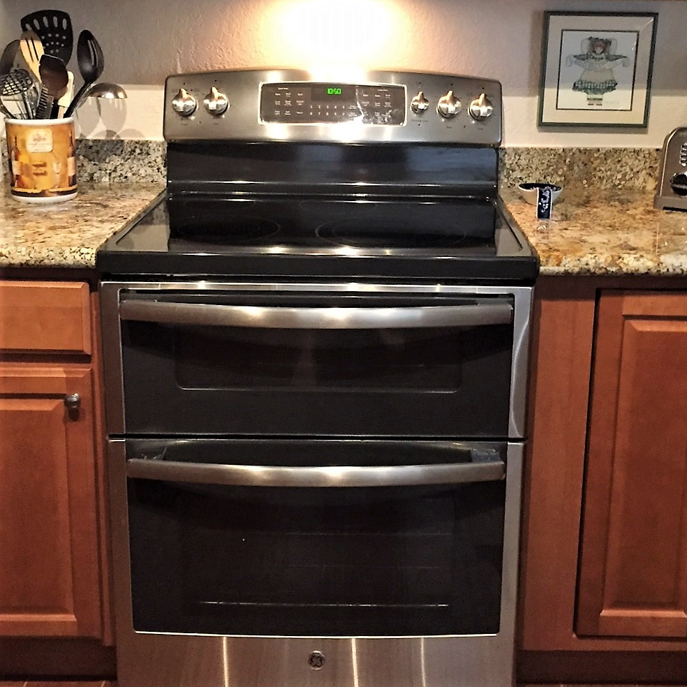 Black and stainless oven and range, Certified by ENERGY STAR, stands between kitchen counters and cabinets; counter holds decorative items and untensils/appliance - photo