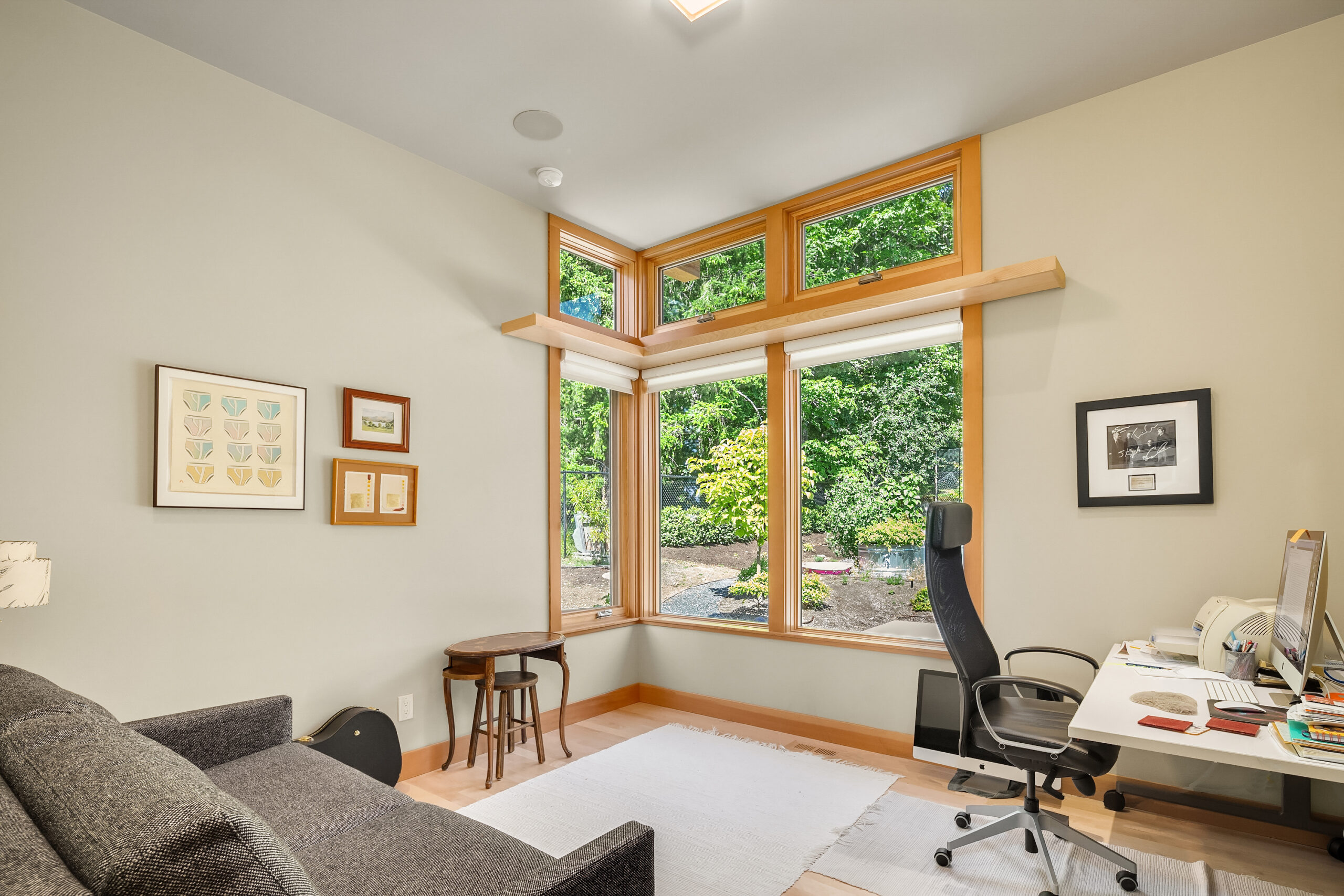 interior view of small home office; desk and chair with computer leave room for foldout couch allowing for use as guest room; ample windows open the space to the outdoors foliage - photo