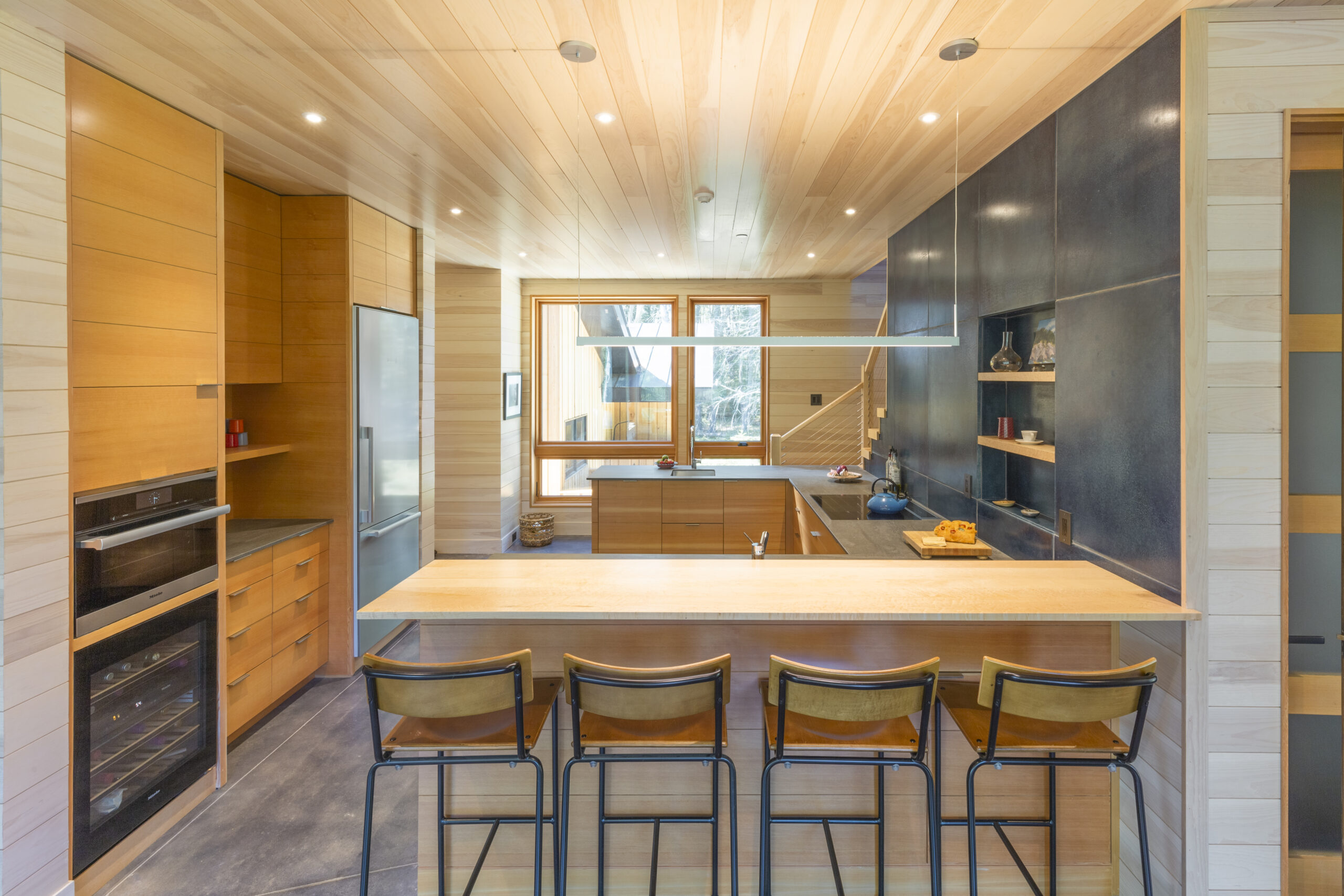 interior view of modern small home-kitchen with dining counter and barstools; striking natural wood ceiling and plenty of built-in storage - photo